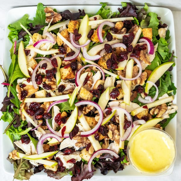 Overhead view of a salad with chicken, apples, cranberries, walnuts, red onion, and croutons.