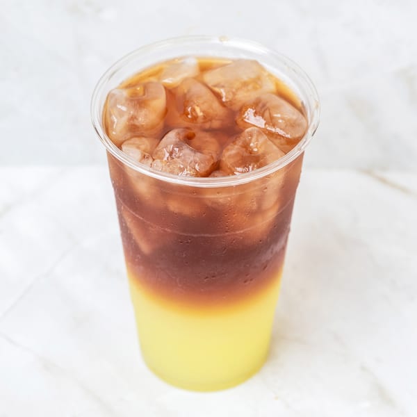 Iced coffee with a layer of yellow juice at the bottom in a clear plastic cup.