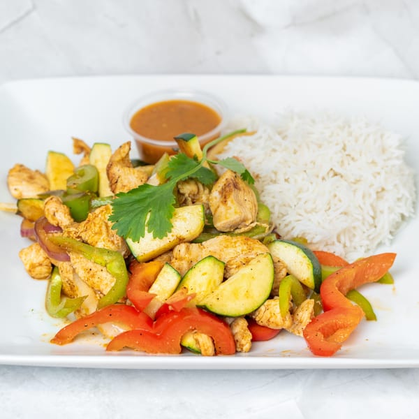 Chicken stir-fry with zucchini, bell peppers, and onions, served with white rice and a side sauce.